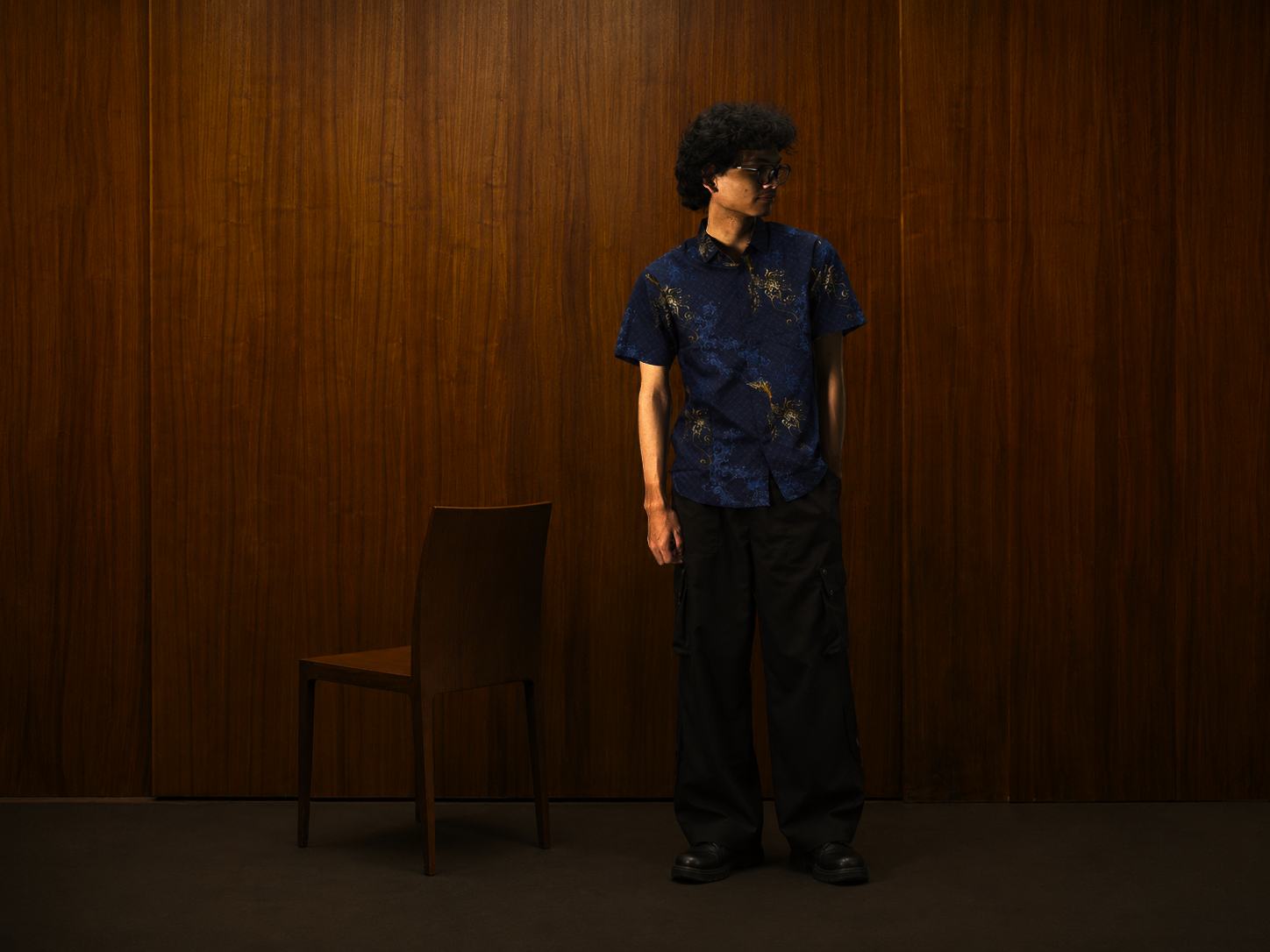 Model mengenakan kemeja batik Santoso navy di depan panel kayu